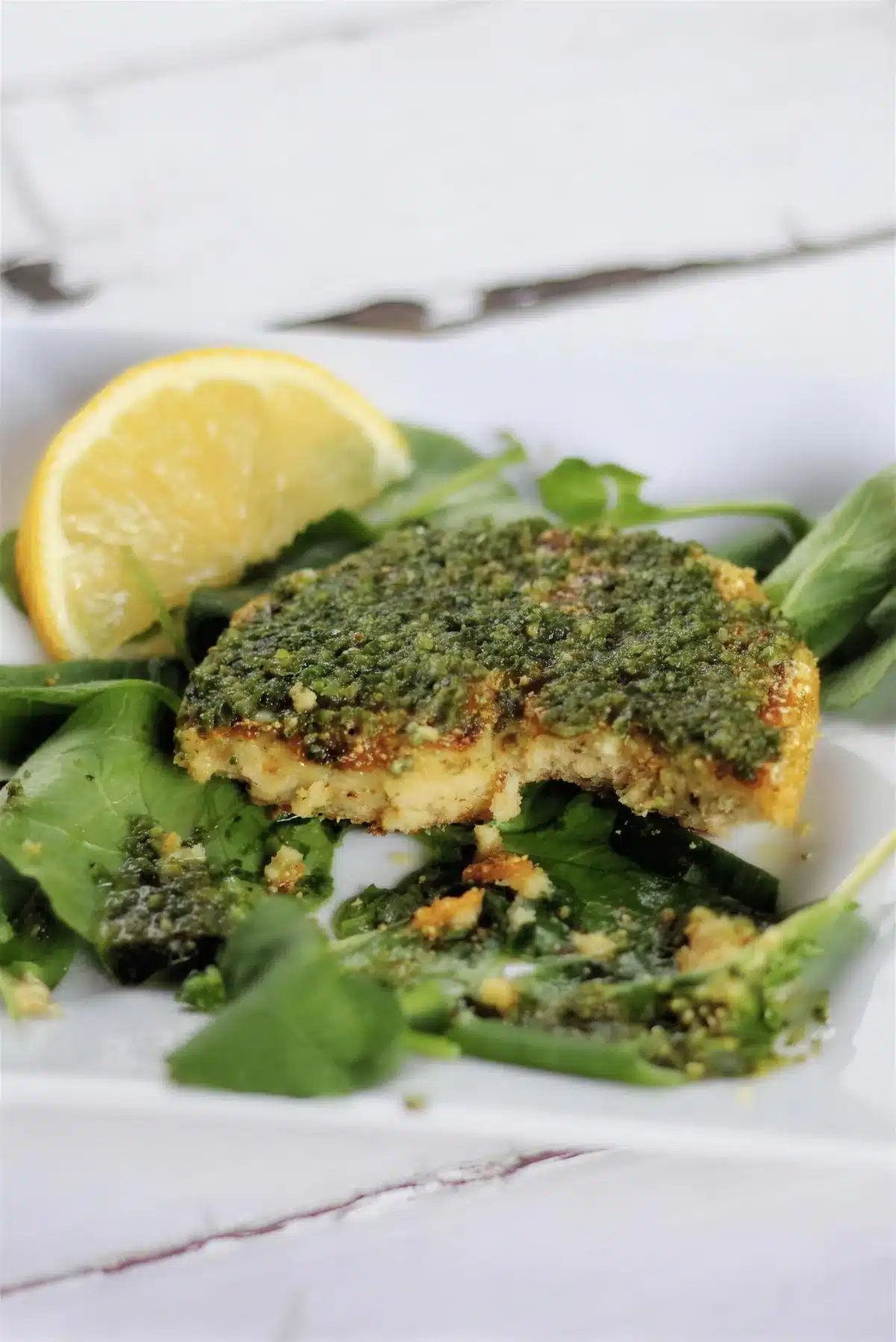 Chickpea patties topped with spicy herb sauce on salad leaves with a lemon wedge