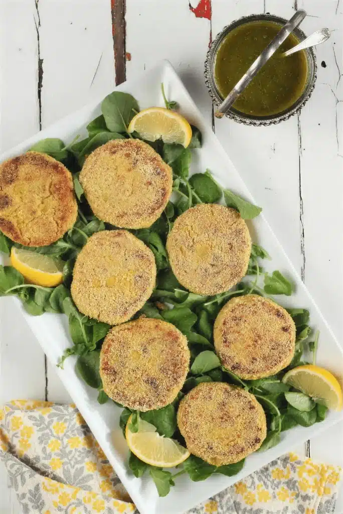 Overhead platter of golden cornmeal crusted rounds on greens with lemon wedges