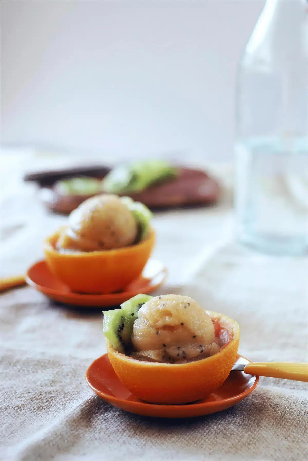 Kiwi sorbet served in two hollowed citrus shells on small orange saucers