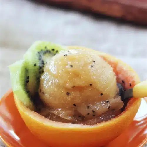 A close scoop of pale frozen dessert in an orange peel cup with a yellow spoon