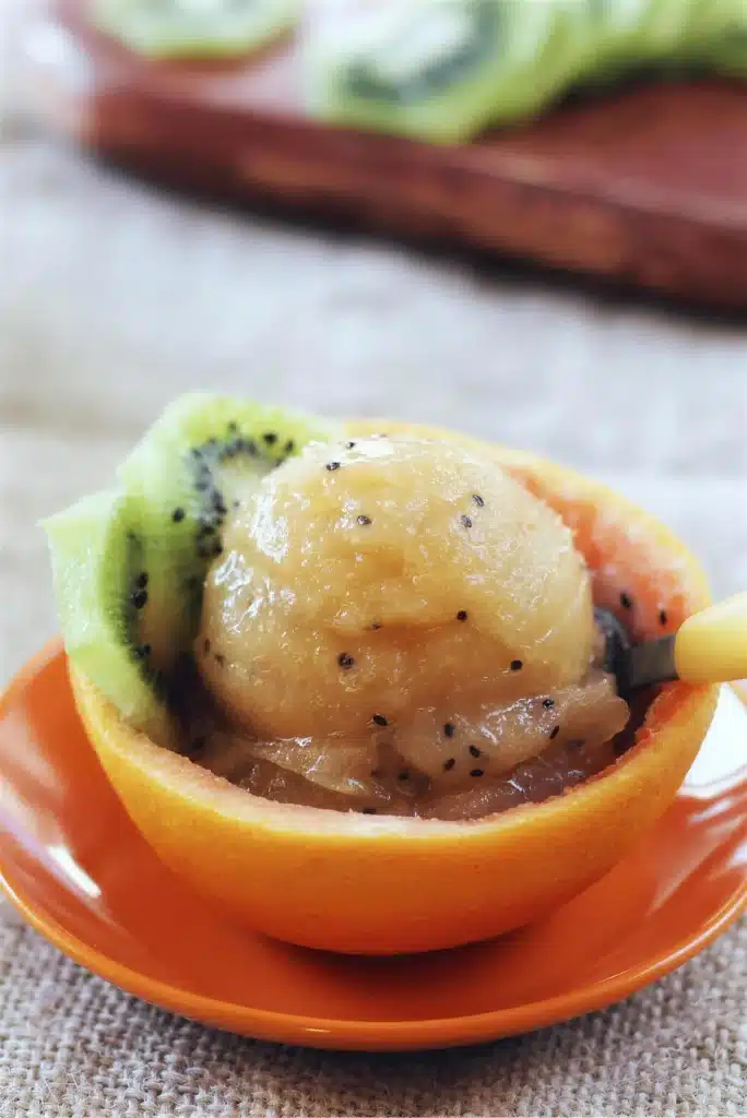 A close scoop of pale frozen dessert in an orange peel cup with a yellow spoon