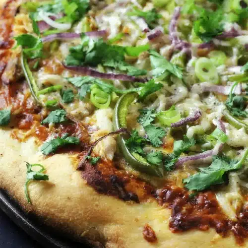 BBQ chicken pizza on a dark pan with a golden puffed crust