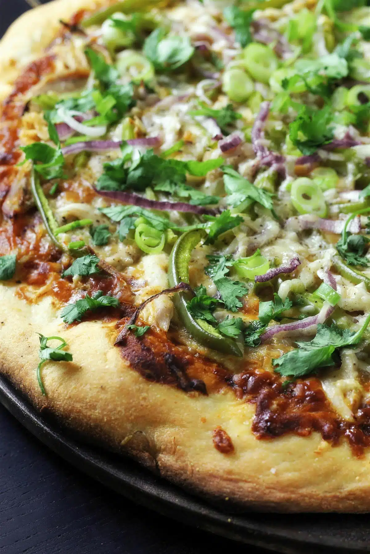 BBQ chicken pizza on a dark pan with a golden puffed crust