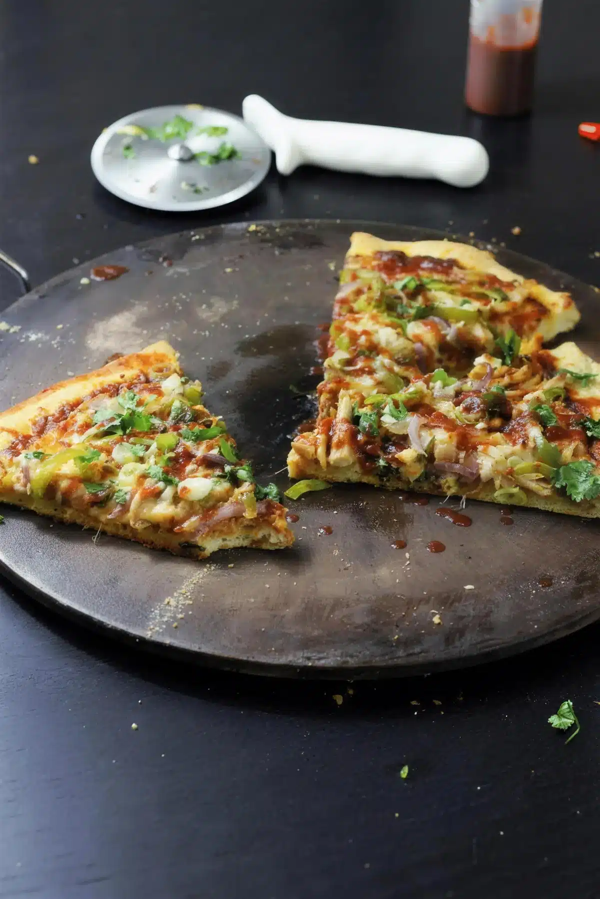 BBQ chicken pizza cut into slices on a dark pan with a serving spoon