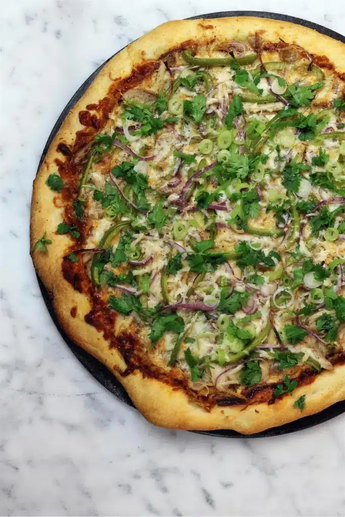 Overhead view of a round flatbread topped with green peppers, red onion and herbs on marble