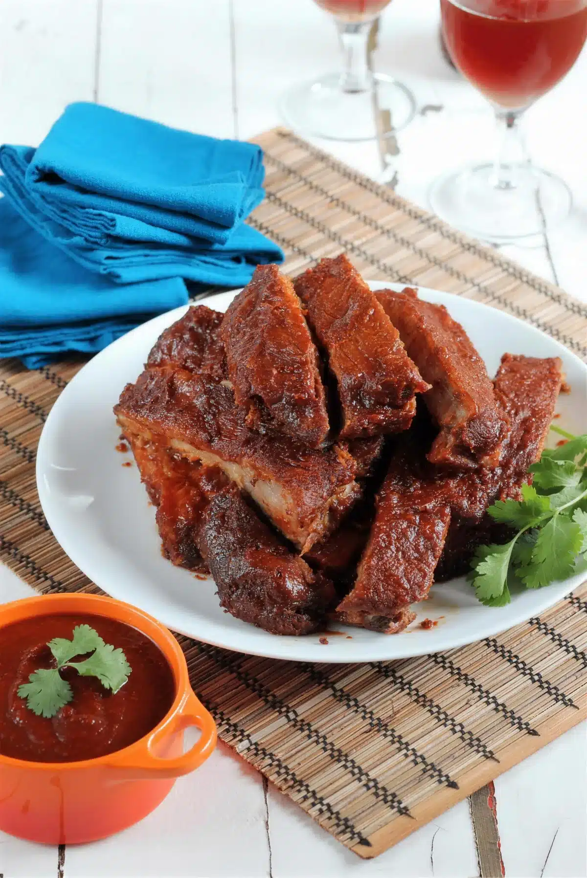 BBQ spare ribs sliced and plated with a small pot of sauce and a blue napkin