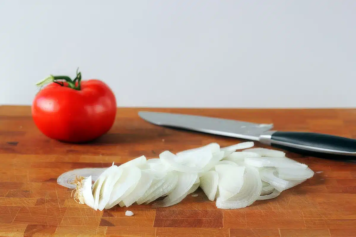 A whole tomato and a heap of thinly sliced onion on a wooden board
