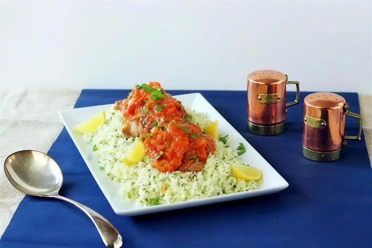 Braised chicken thighs plated on a blue cloth beside two small copper mugs