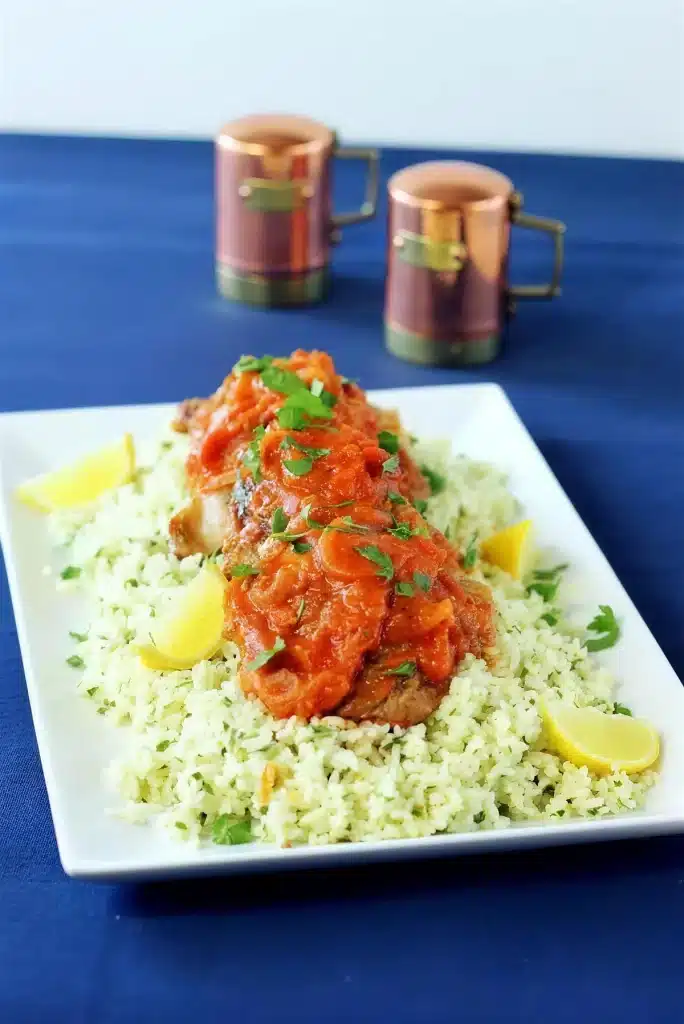 Saucy poultry served over herbed couscous with lemon on a white plate