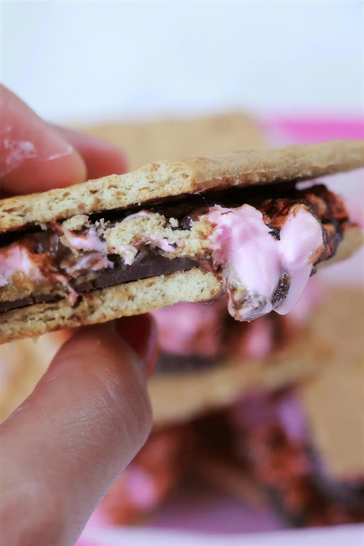 Peanut butter smores held up so the pink marshmallow squeezes out the side