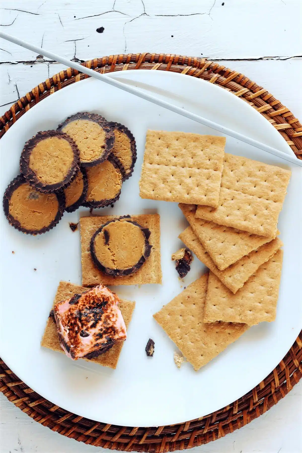 Chocolate cups, graham crackers and one toasted marshmallow on a white plate