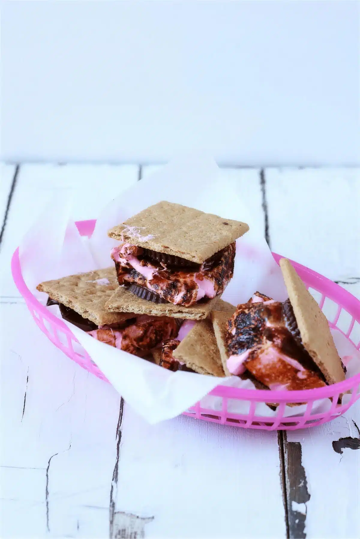 Toasted marshmallow sandwiches piled in a pink basket on white boards