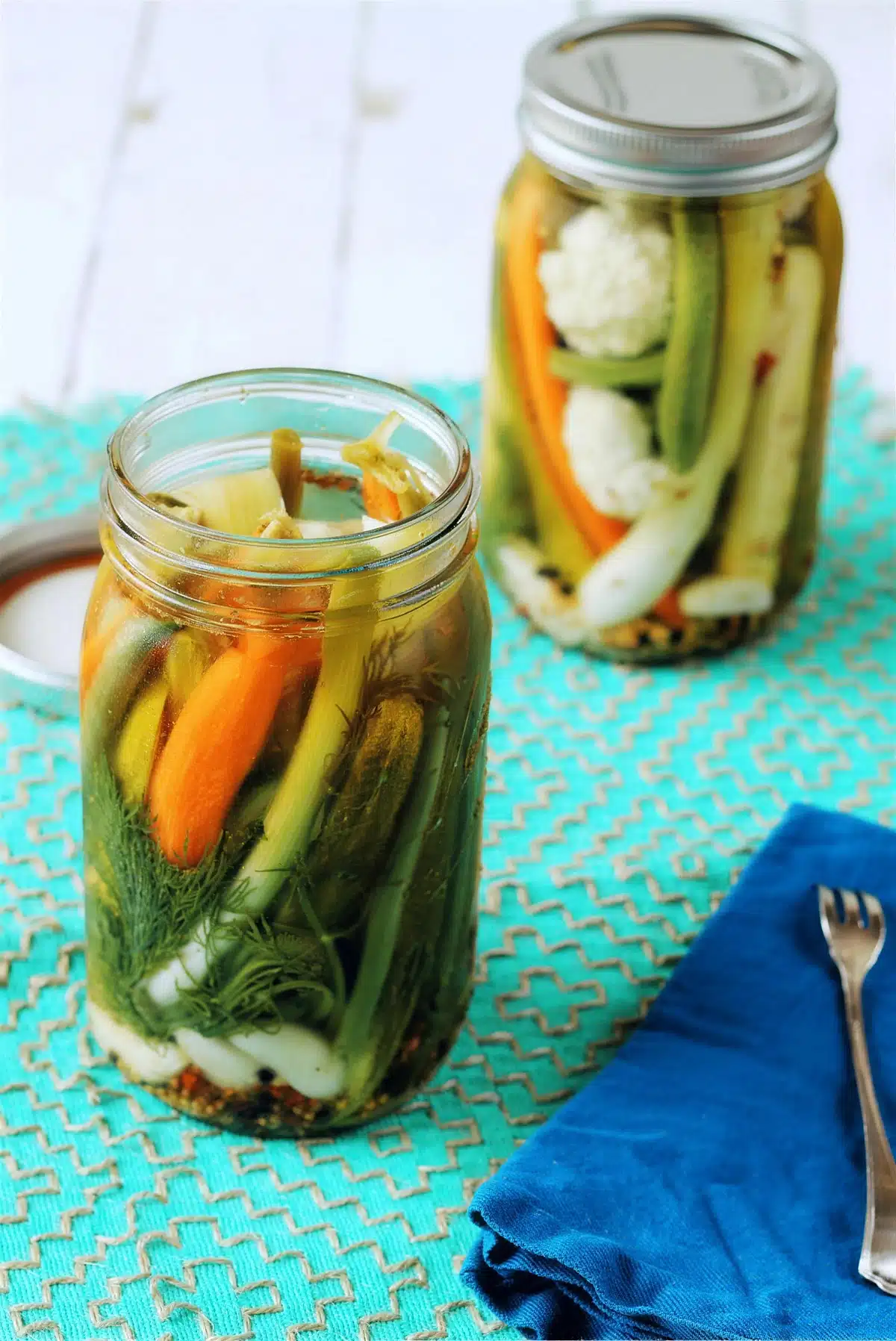 Pickled vegetables in two jars on a turquoise mat