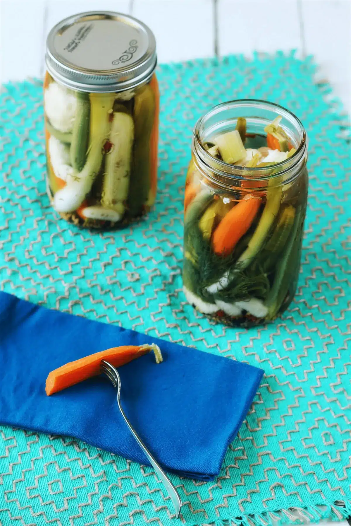 Pickled vegetables in two jars with a blue napkin and a fork alongside