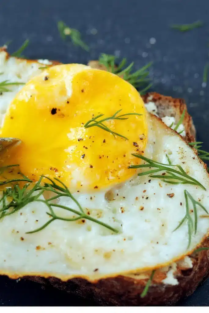 Close up of a runny yolk and dill on a thick slice of toasted country bread
