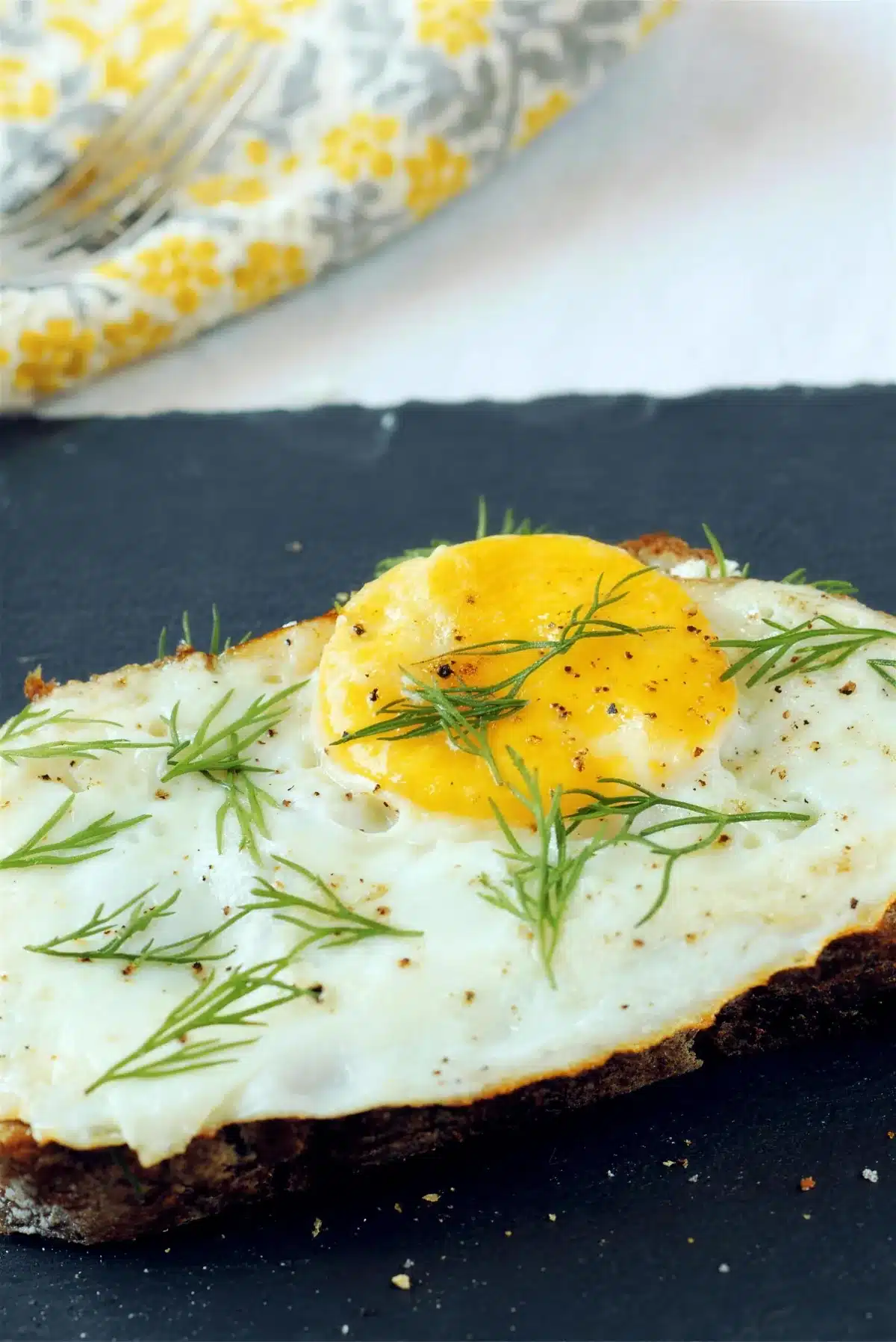 Open faced egg sandwich on dark slate with a runny yolk and fresh dill