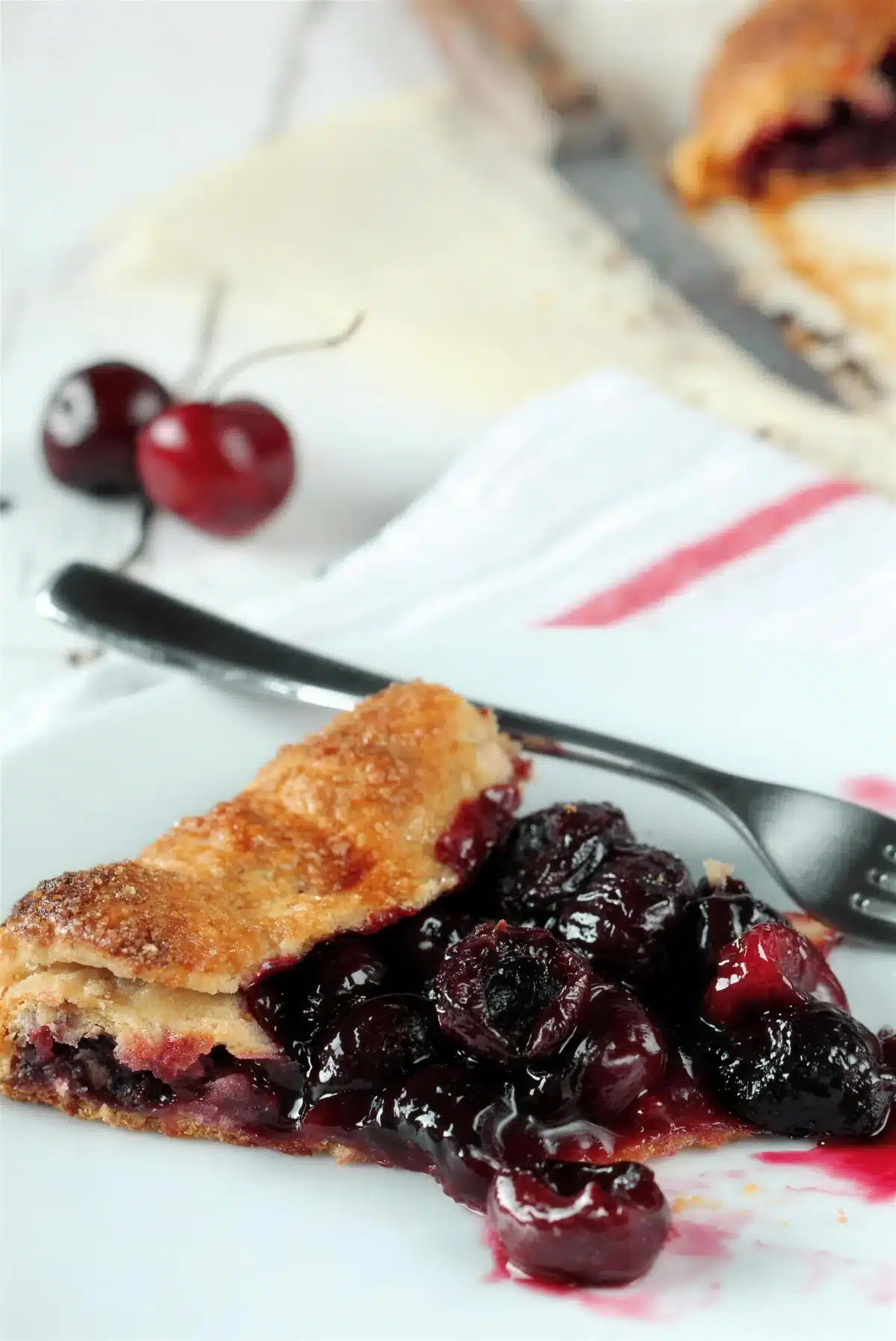 Cherry galette slice on a plate with a fork and a striped napkin behind it
