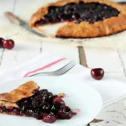 Cherry galette on parchment with one slice lifted onto a white plate