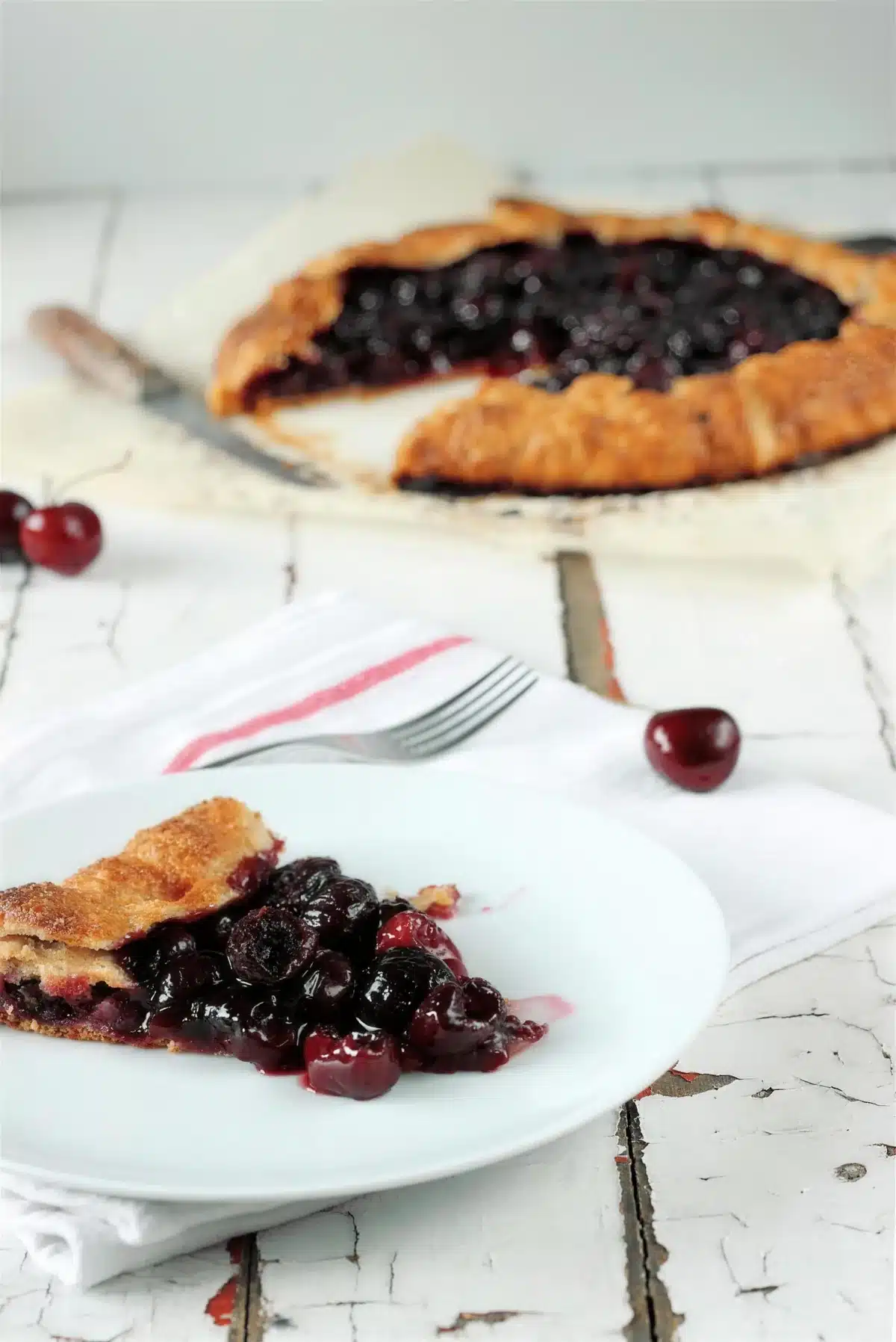 Cherry galette on parchment with one slice lifted onto a white plate