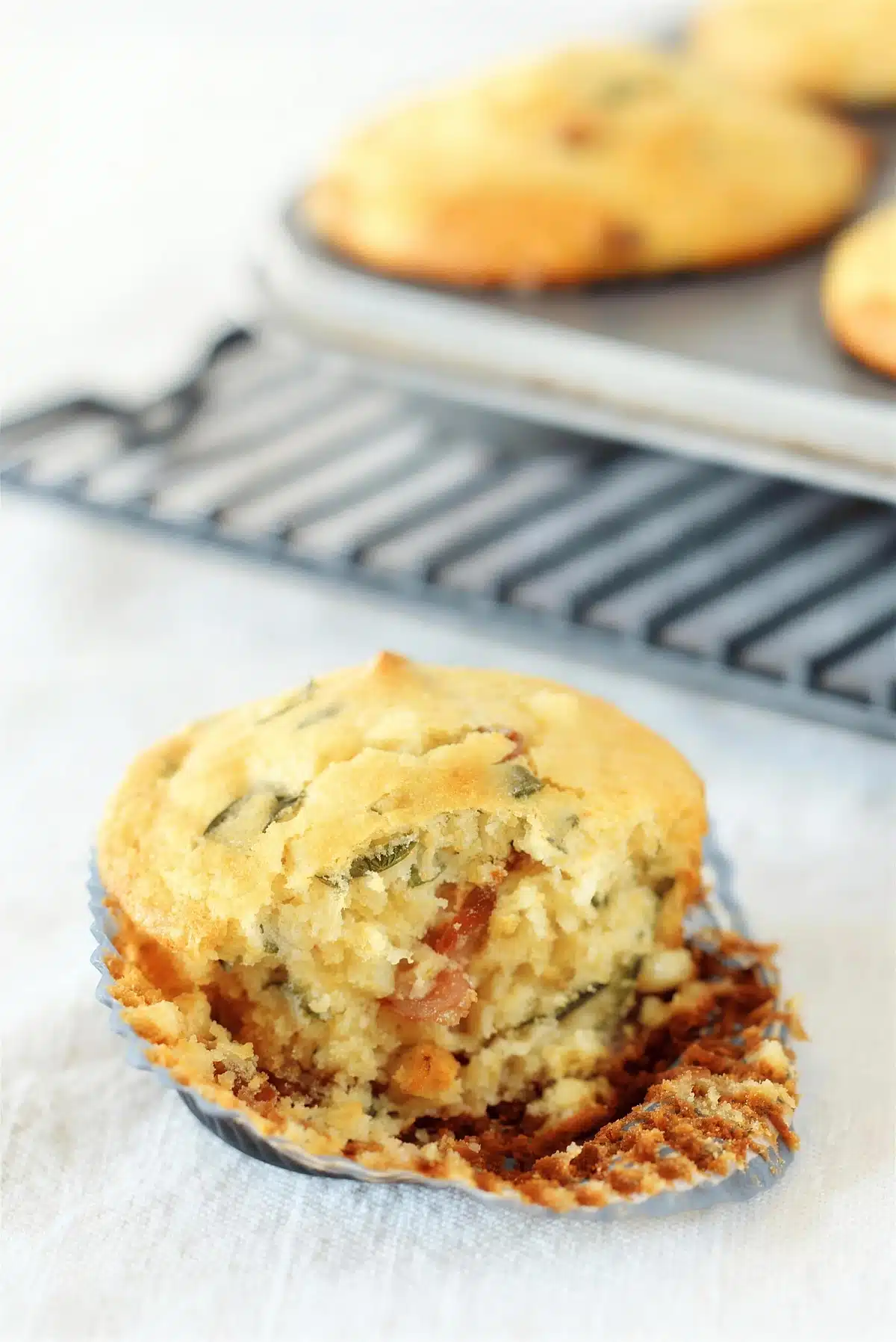 Cornbread muffins split open on a rack to show the bacon and basil in the crumb