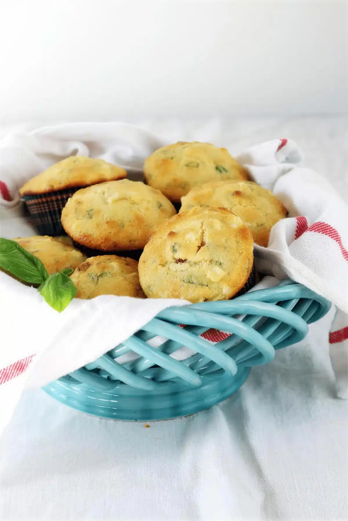 Cornbread muffins piled in a blue basket with a striped cloth and a basil sprig