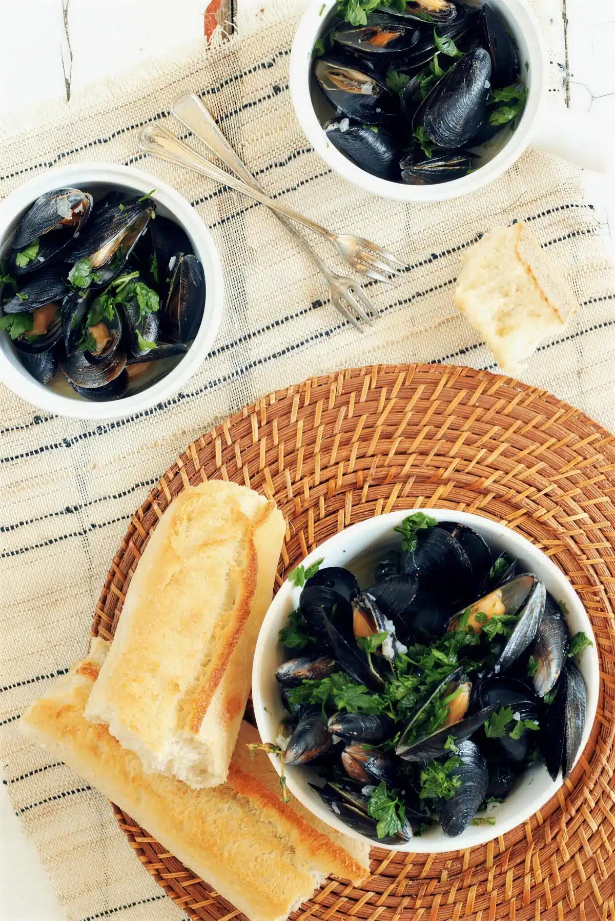Mussels in white wine served in two bowls with baguette alongside