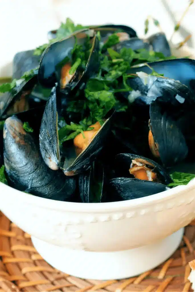 Mussels in white wine steamed open in a white bowl with parsley