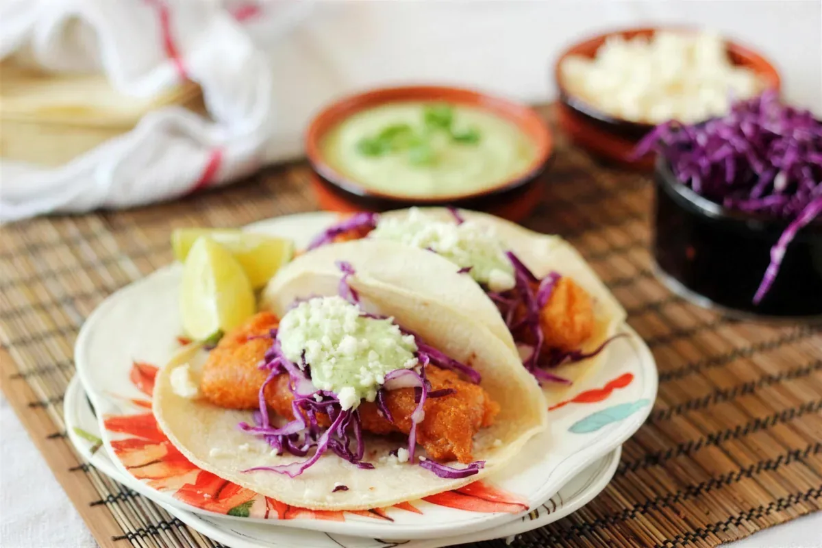 Beer battered fish tacos on a painted plate with lime and crema