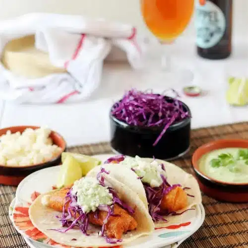 Beer battered fish tacos on a plate with cabbage slaw, crema and a cold beer