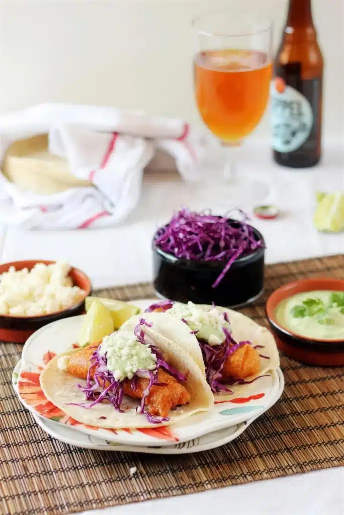 Beer battered fish tacos on a plate with cabbage slaw, crema and a cold beer