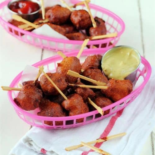 Mini corn dogs in a pink basket with mustard and ketchup