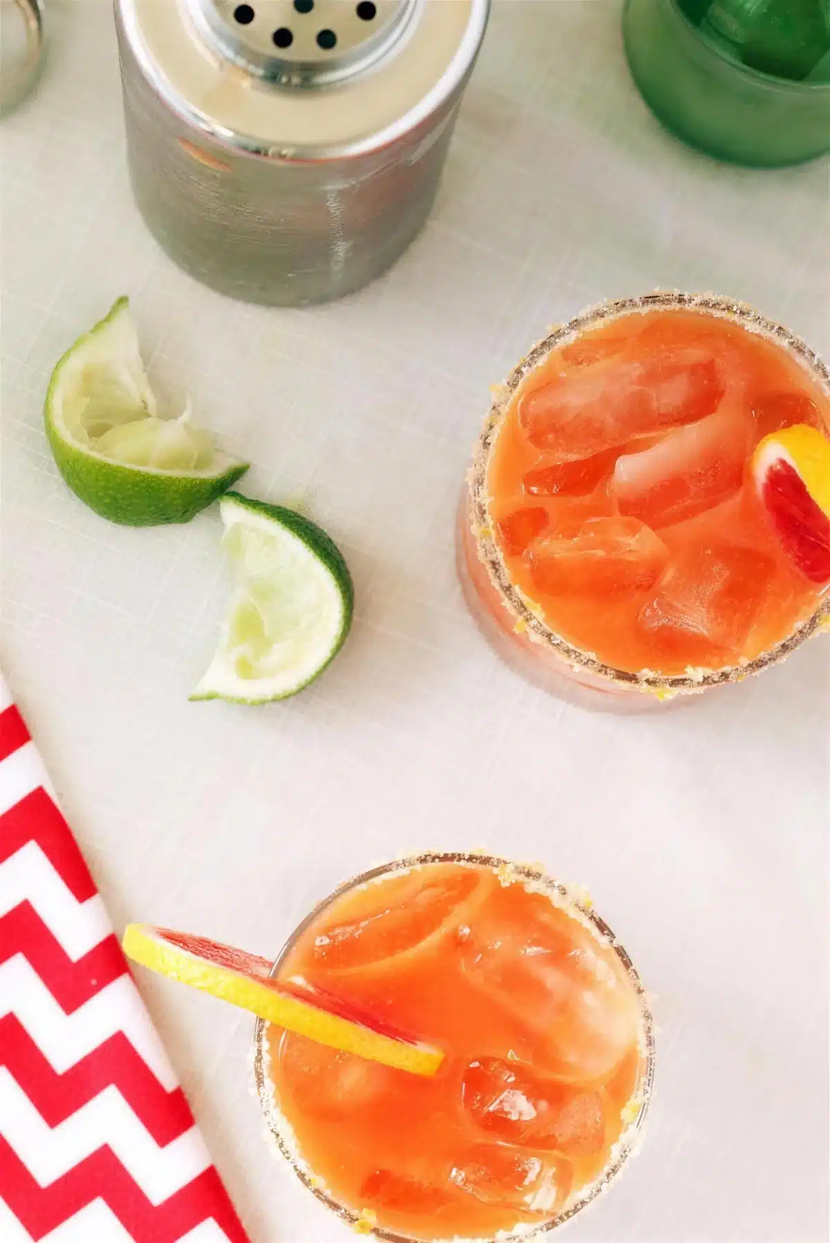 Blood orange cocktail seen from above with lime wedges on a chevron cloth