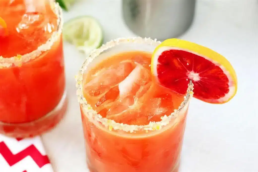 Two sugar-rimmed glasses of ruby drink garnished with a citrus wheel