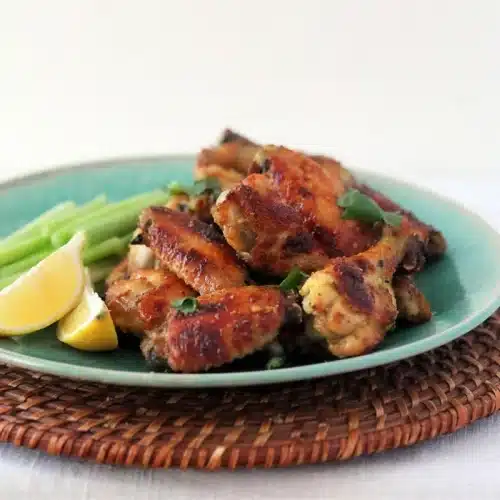 Indian chicken wings piled on a teal plate with celery sticks and lemon wedges