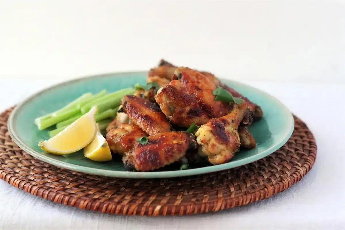 Indian chicken wings piled on a teal plate with celery sticks and lemon wedges