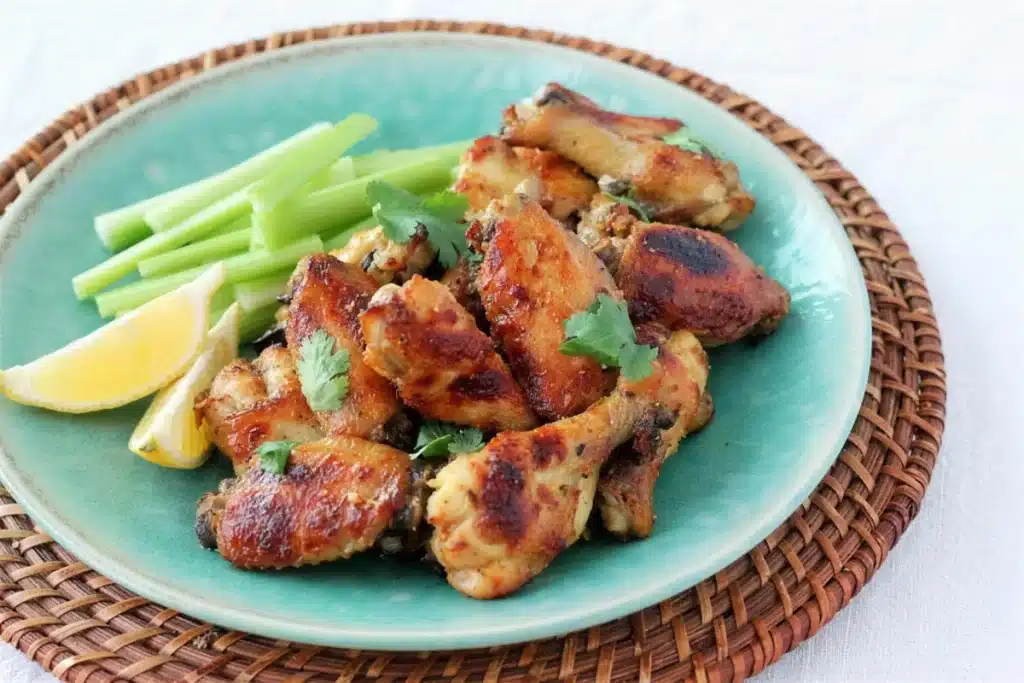 Roasted poultry pieces with celery sticks and lemon on a teal plate