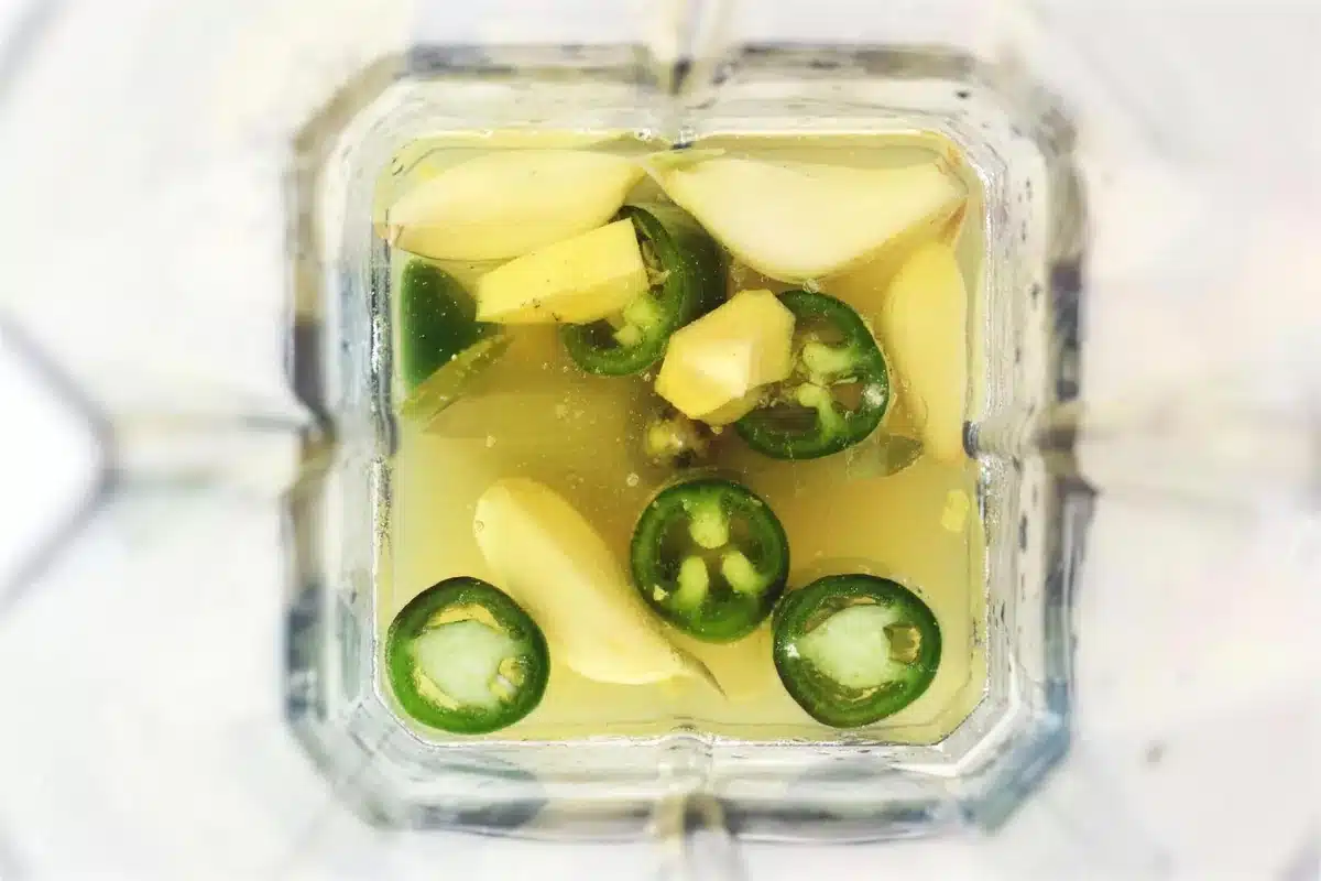 Ginger, garlic and sliced green chile floating in lemon juice in a blender jar