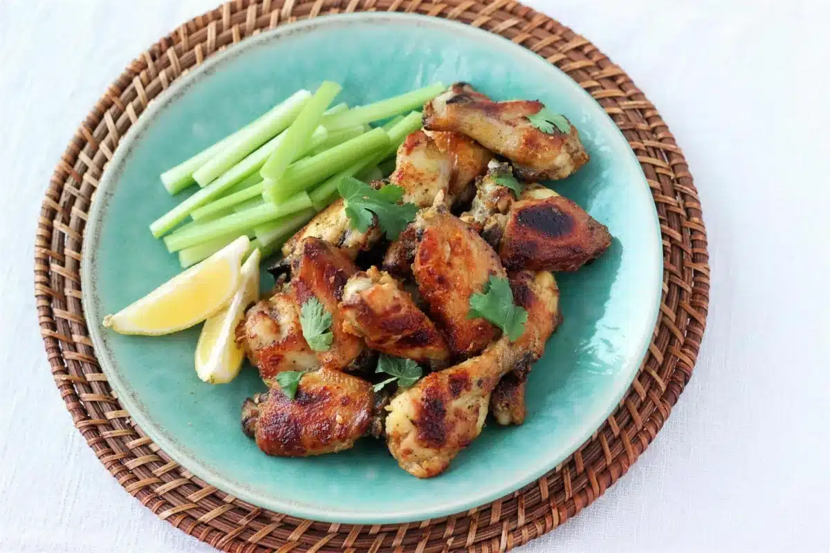 Crisp indian chicken wings served with celery and lemon on a pale green plate