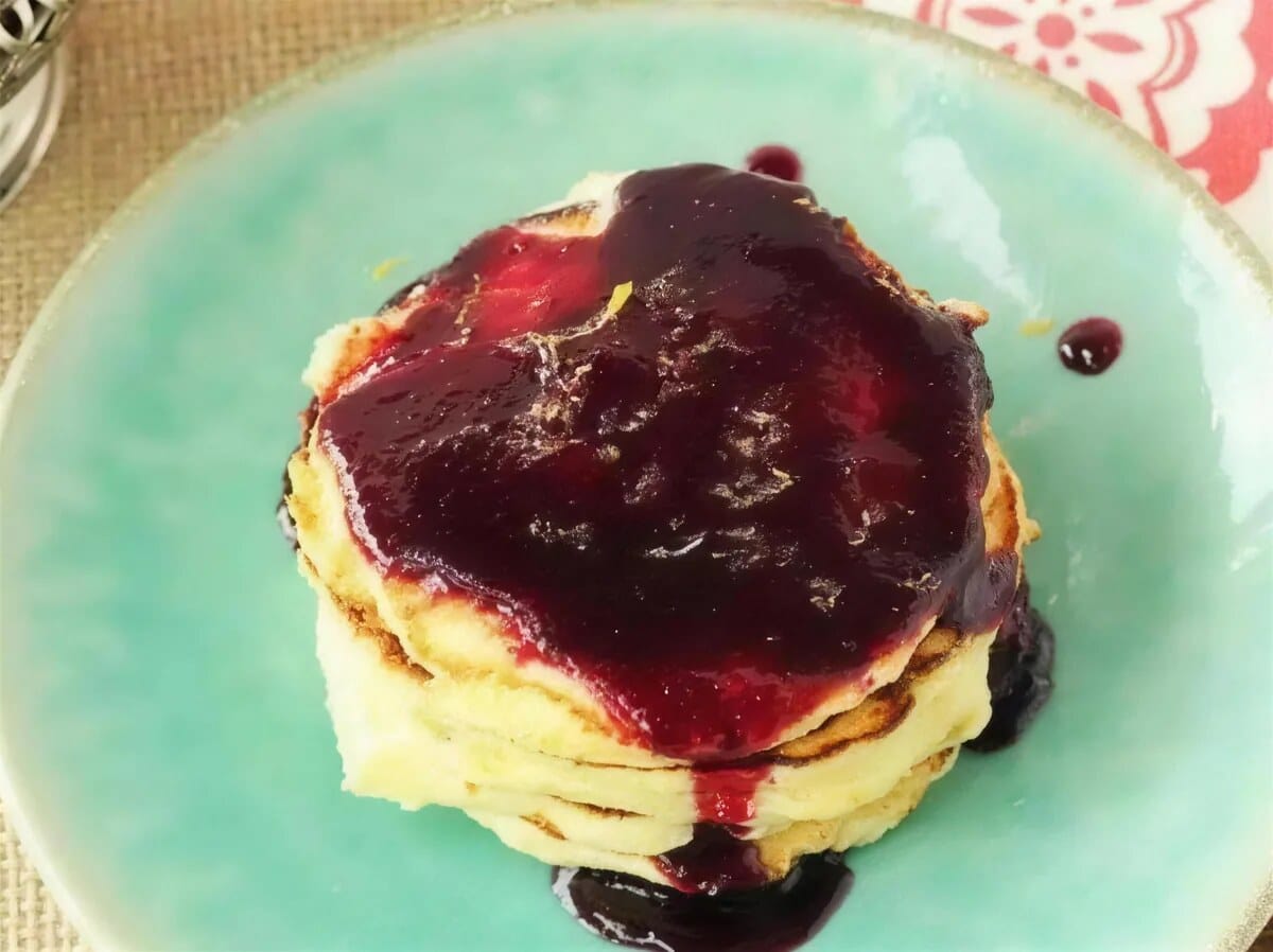 Warm berry sauce running down the sides of a stack on a teal plate