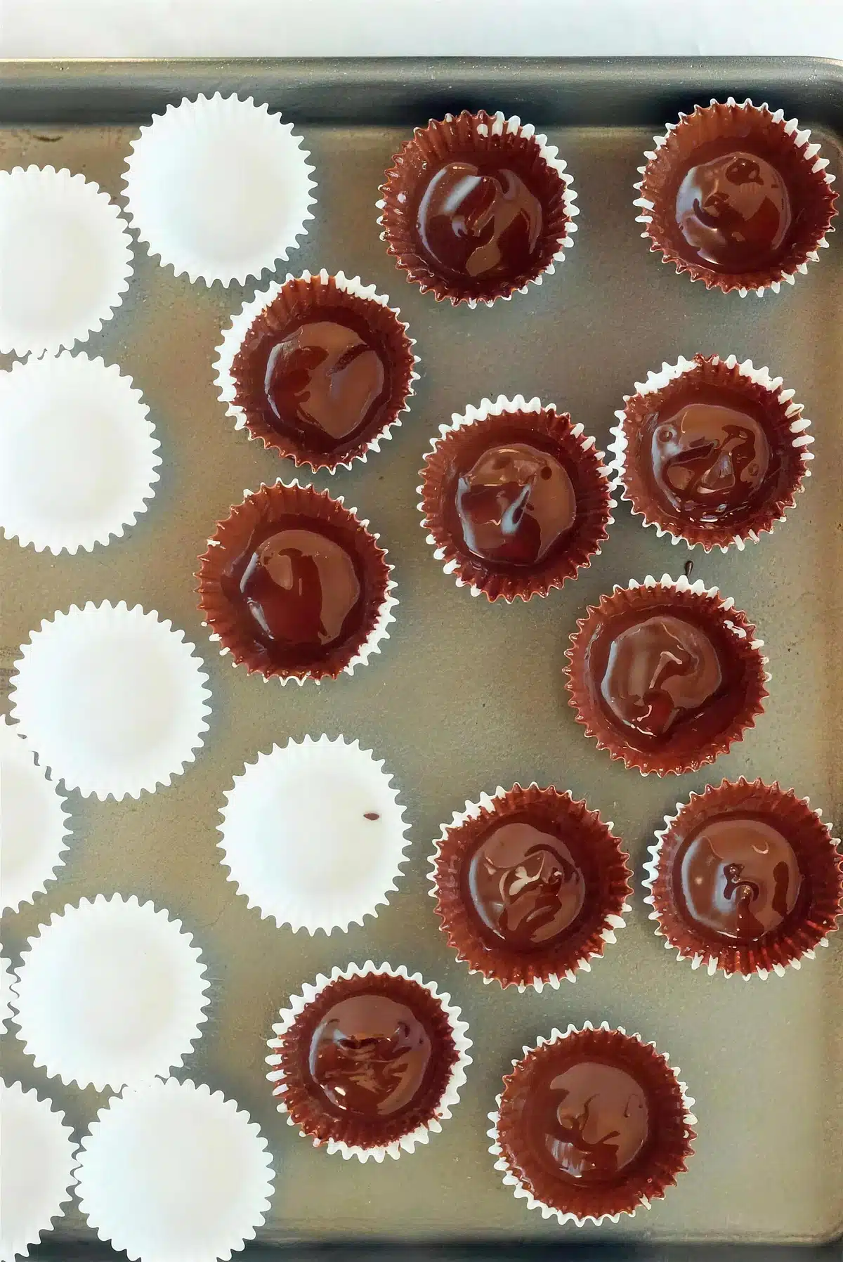 Melted chocolate painted into mini foil liners lined up on a metal tray