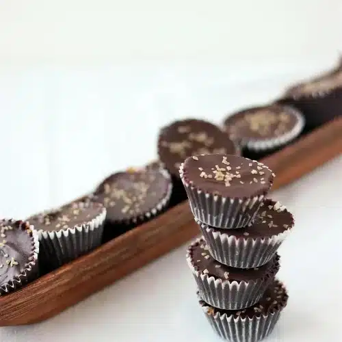 Homemade peanut butter cups stacked beside more candies on a wooden tray