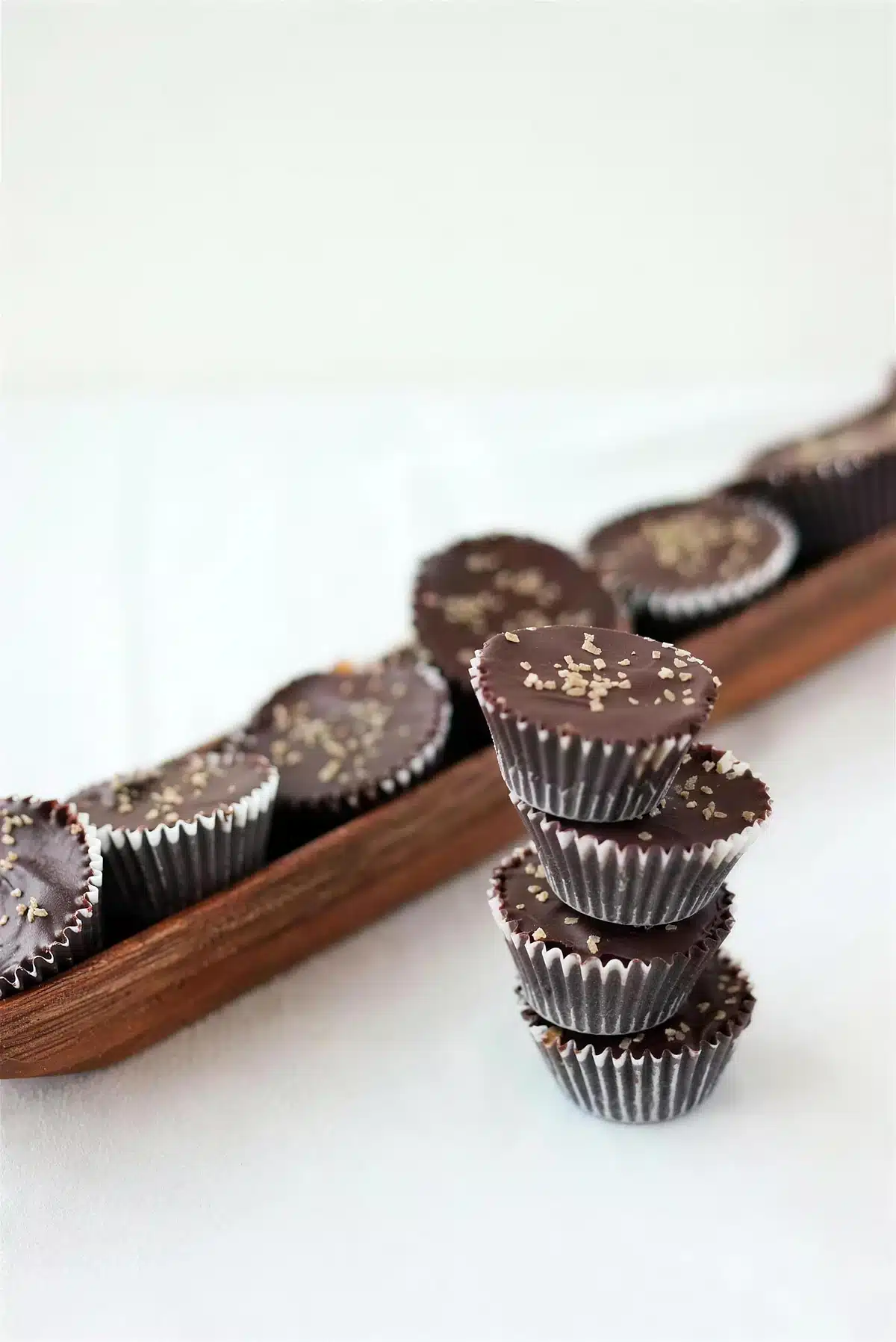 Homemade peanut butter cups stacked beside more candies on a wooden tray