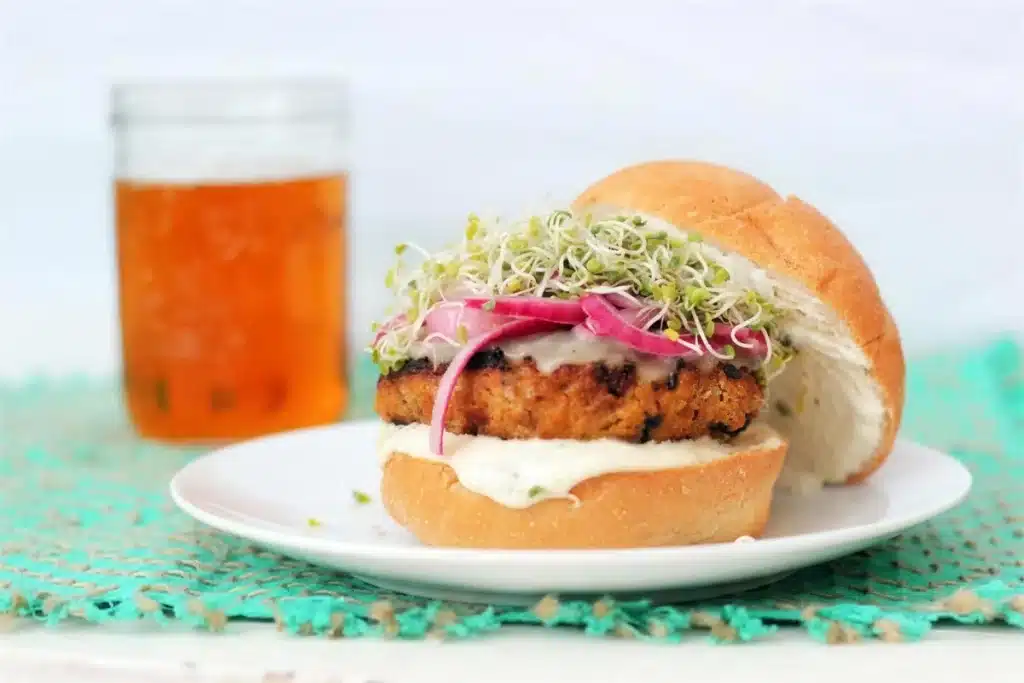Sandwich on a white plate with sprouts and pickled onion, a jar of iced tea behind