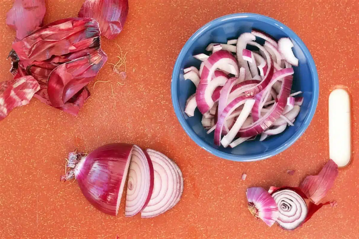Thinly sliced red onion in a blue bowl for a quick pickle to top a turkey burger