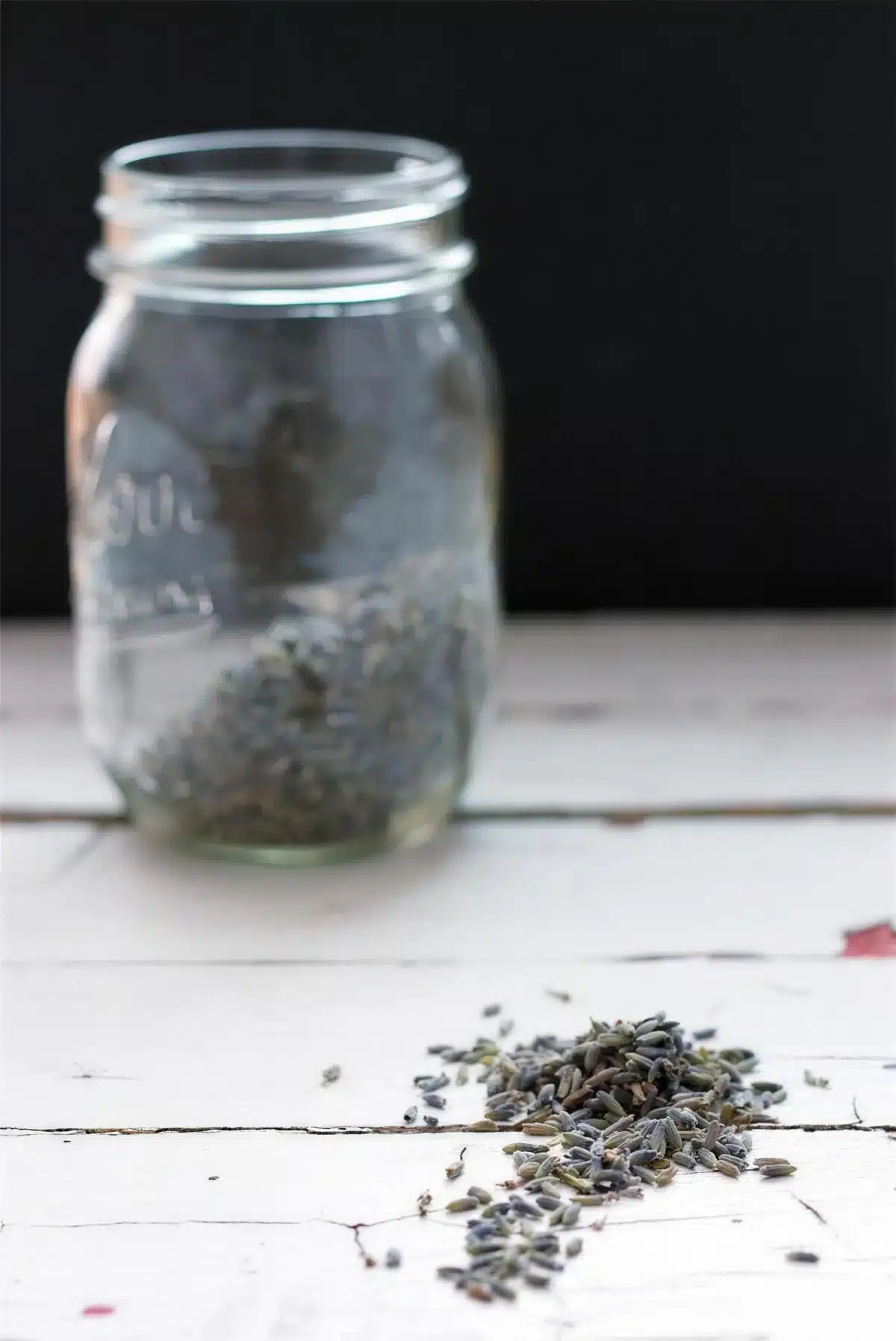 Dried lavender buds in a glass mason jar with more scattered on white wood
