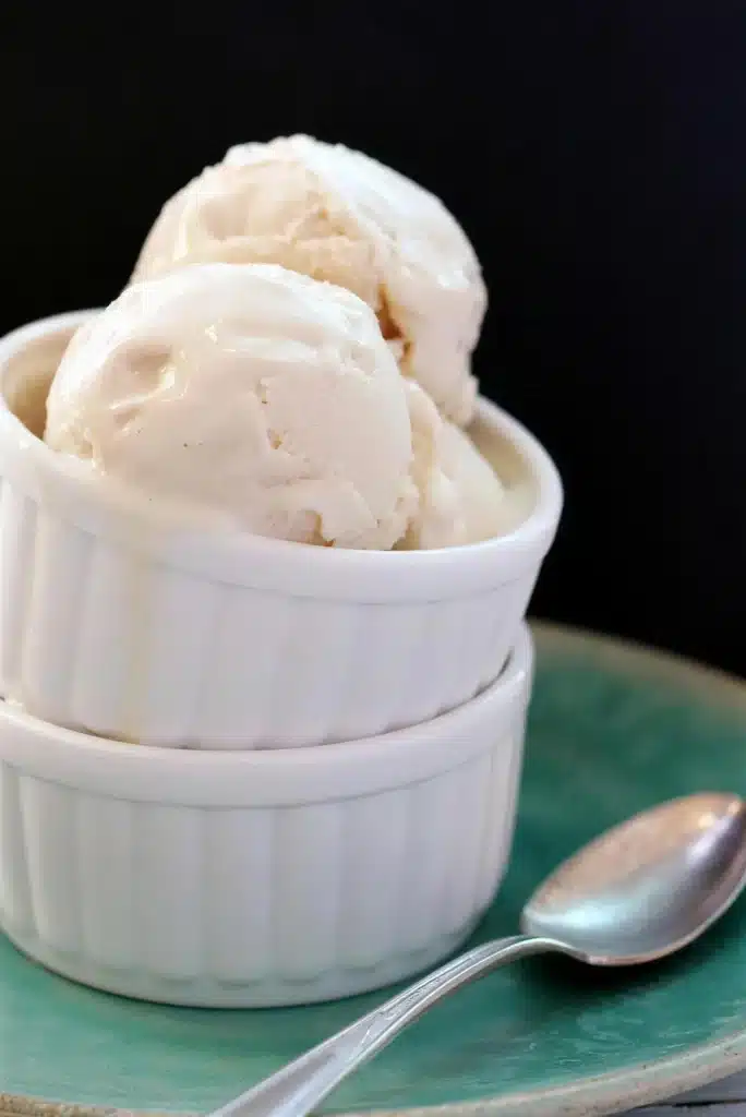Creamy pale scoops in two stacked white ramekins with a spoon alongside