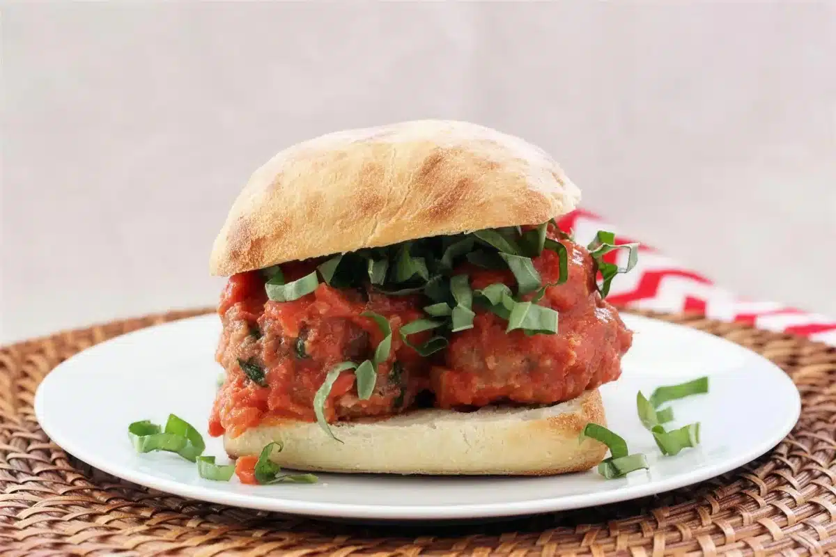 Meatball sandwiches on a woven mat beside a red and white striped cloth