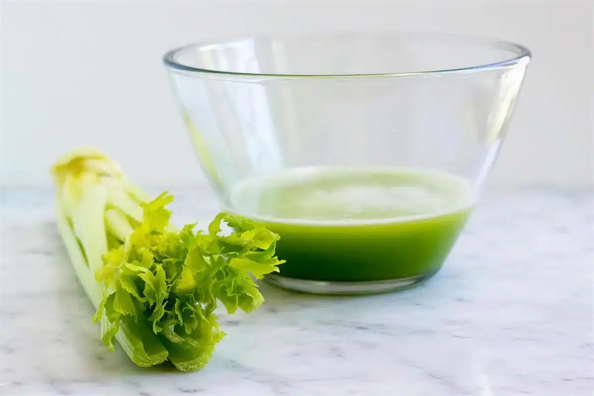 Freshly pressed celery juice in a glass bowl beside trimmed stalks