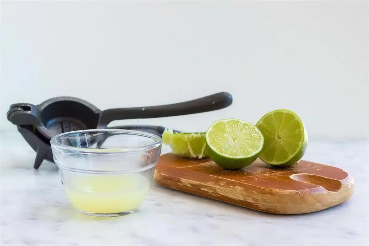 Squeezed lime halves on a wooden board beside a metal press