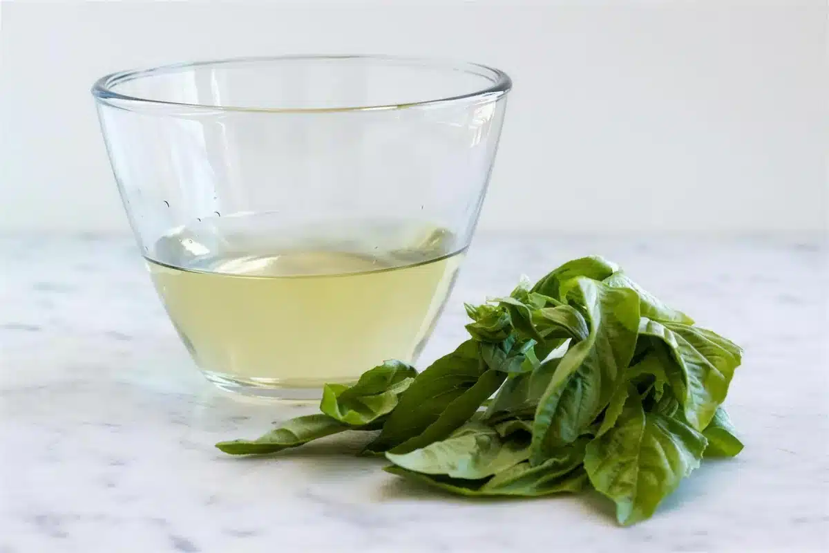 Basil simple syrup cooling in a bowl with a bundle of leaves alongside